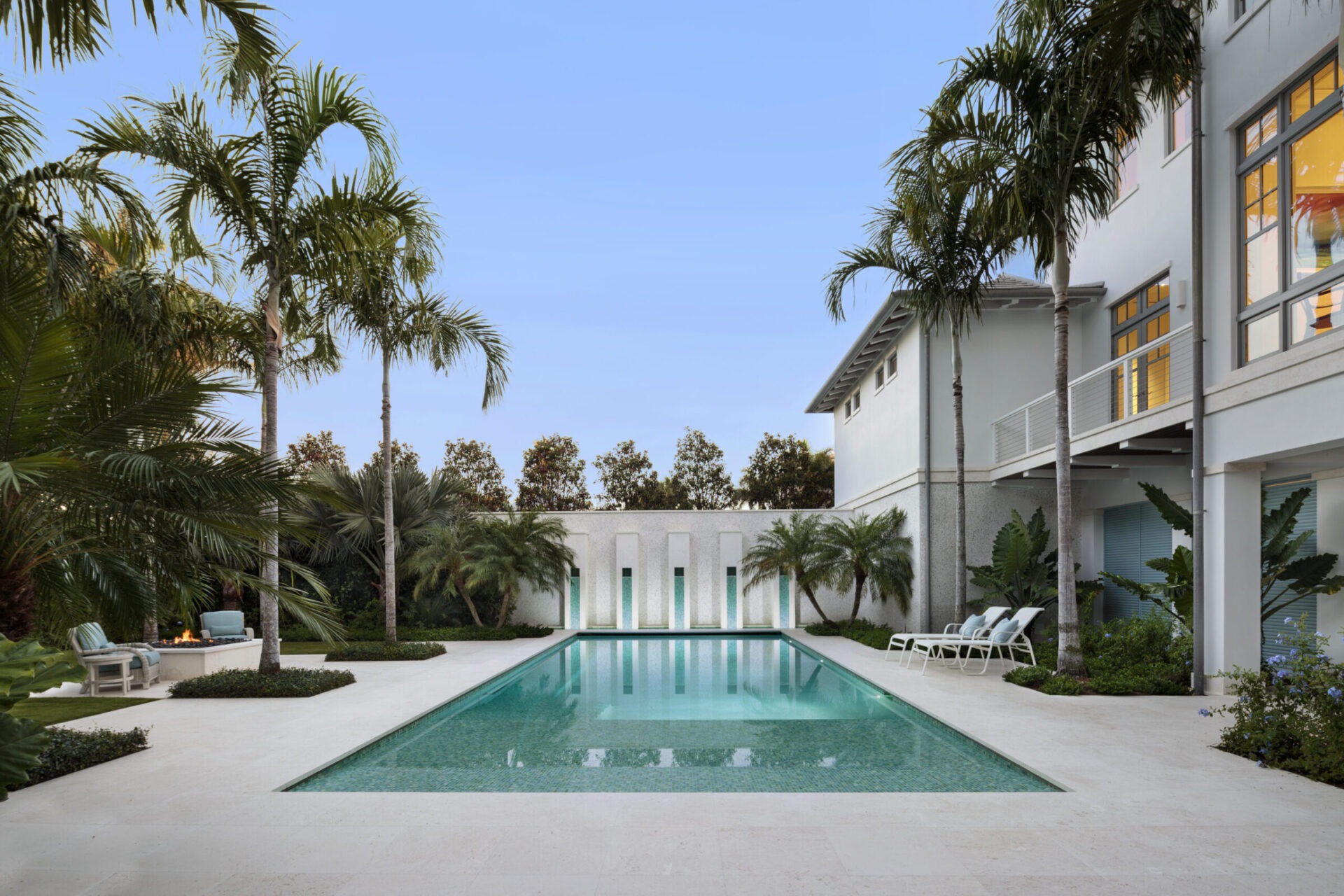 Luxurious outdoor pool surrounded by palm trees, modern architecture, and lounge chairs; serene setting with clear blue sky and landscaped garden.