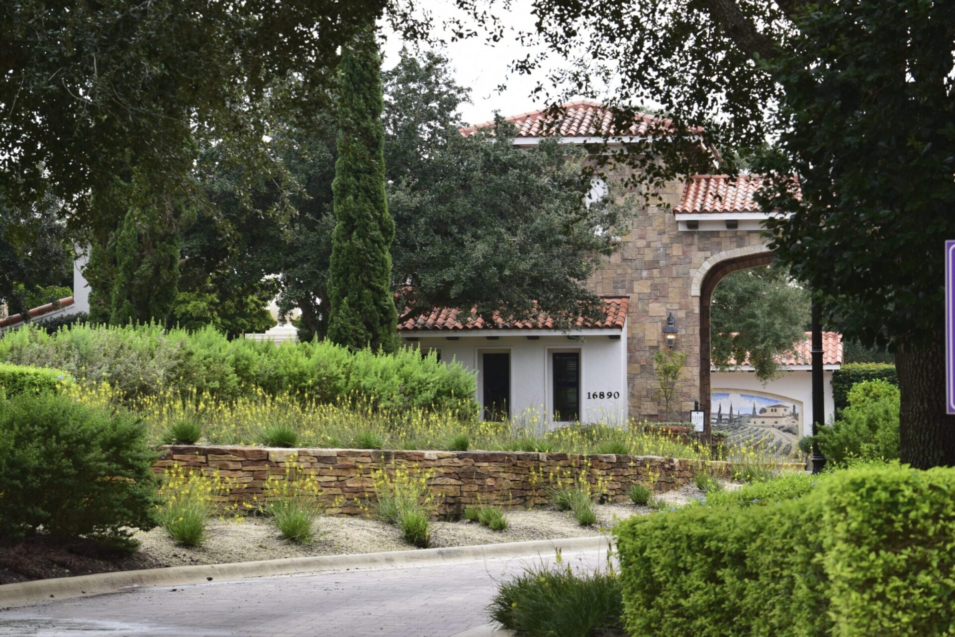 A charming Mediterranean-style house with stone walls and red roof, surrounded by lush greenery and tall trees, evokes a serene atmosphere.