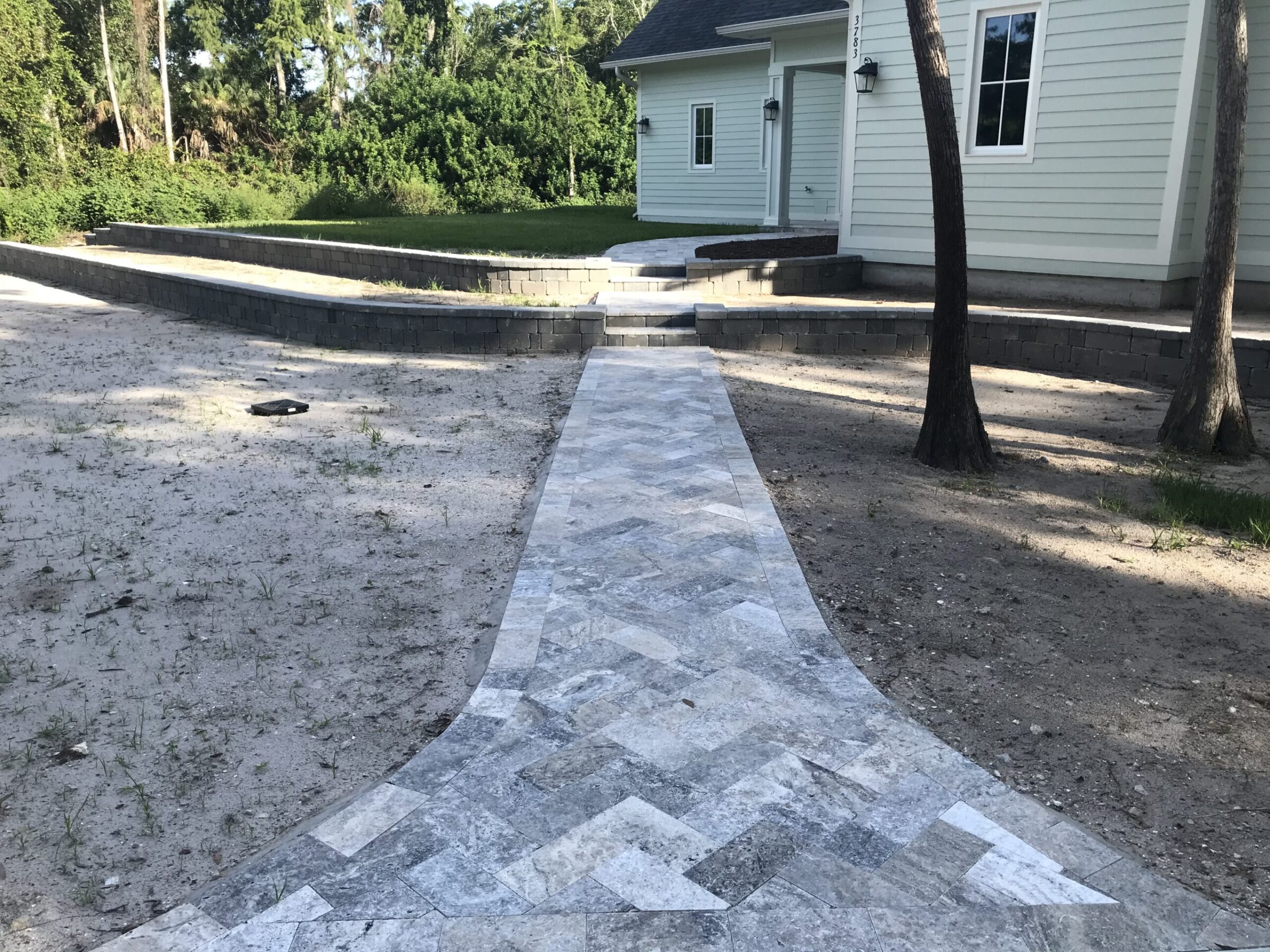 A paved stone pathway leads to a light-colored house surrounded by trees and a shaded yard. No landmarks are visible.