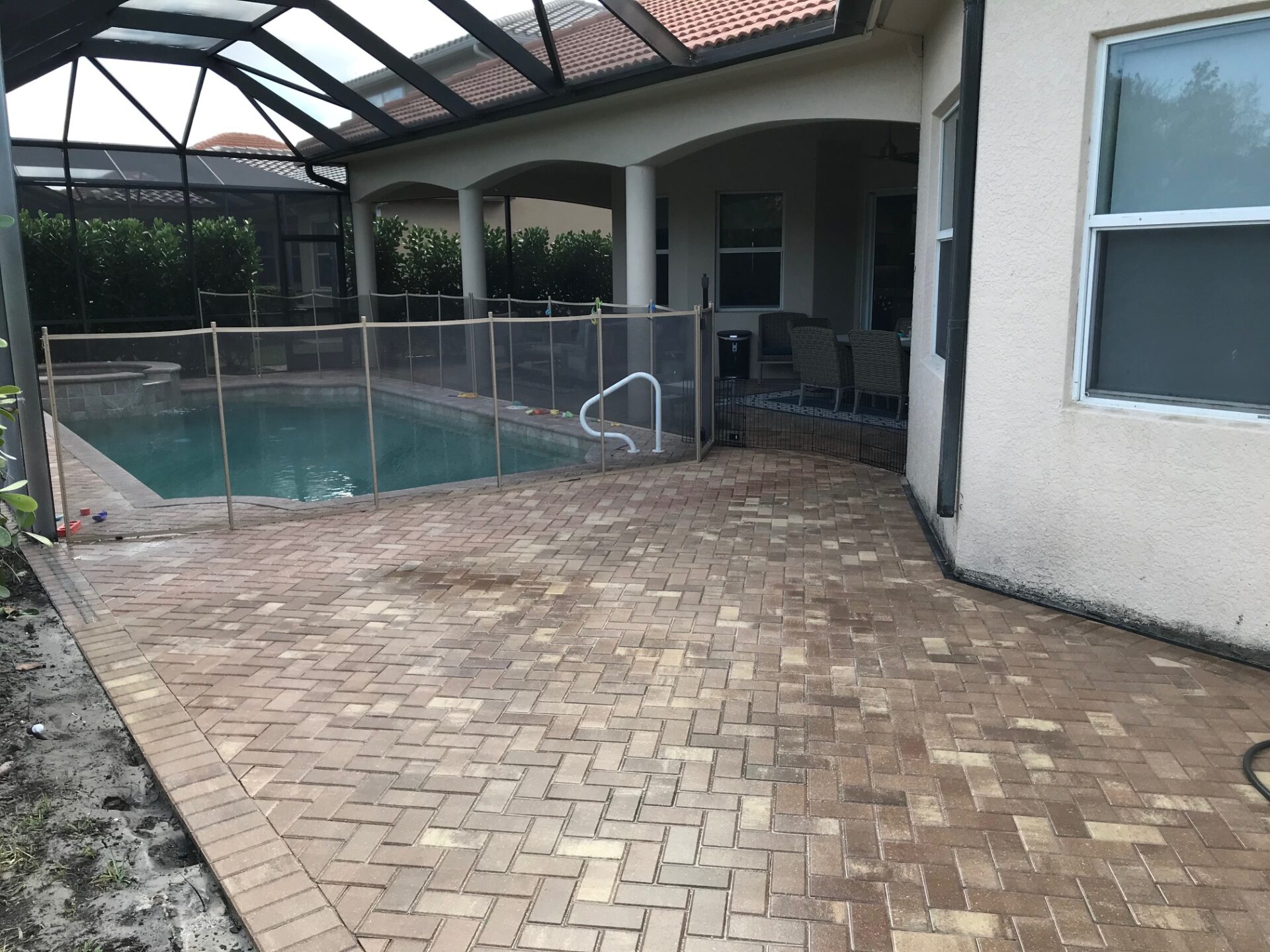 A screened-in patio features a swimming pool, surrounded by a safety fence and brick pavers, adjacent to an outdoor seating area.