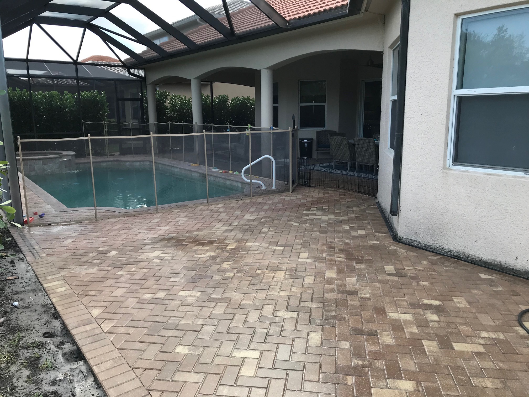 A screened-in patio features a swimming pool, surrounded by a safety fence and brick pavers, adjacent to an outdoor seating area.