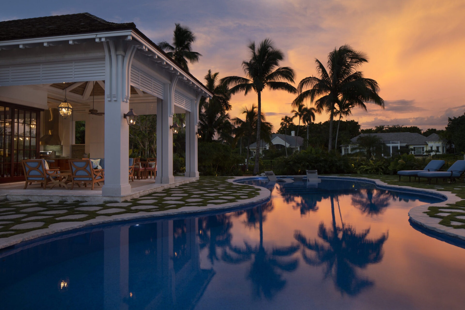 Elegant poolside setting at sunset, featuring lush palm trees and luxurious seating area. Reflections create a tranquil ambiance. No recognizable landmarks present.