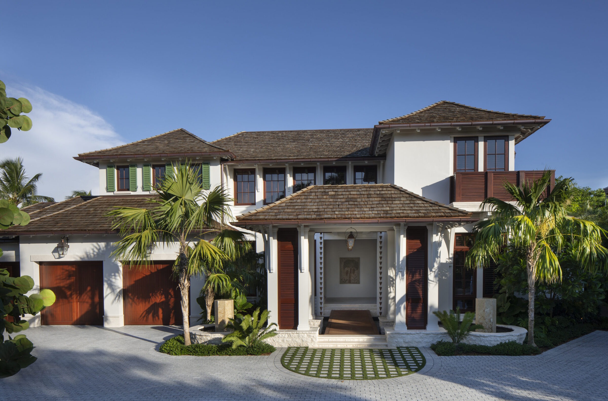 Modern two-story house with wooden accents, surrounded by tropical plants and trees, clear blue sky in the background, creating a serene atmosphere.