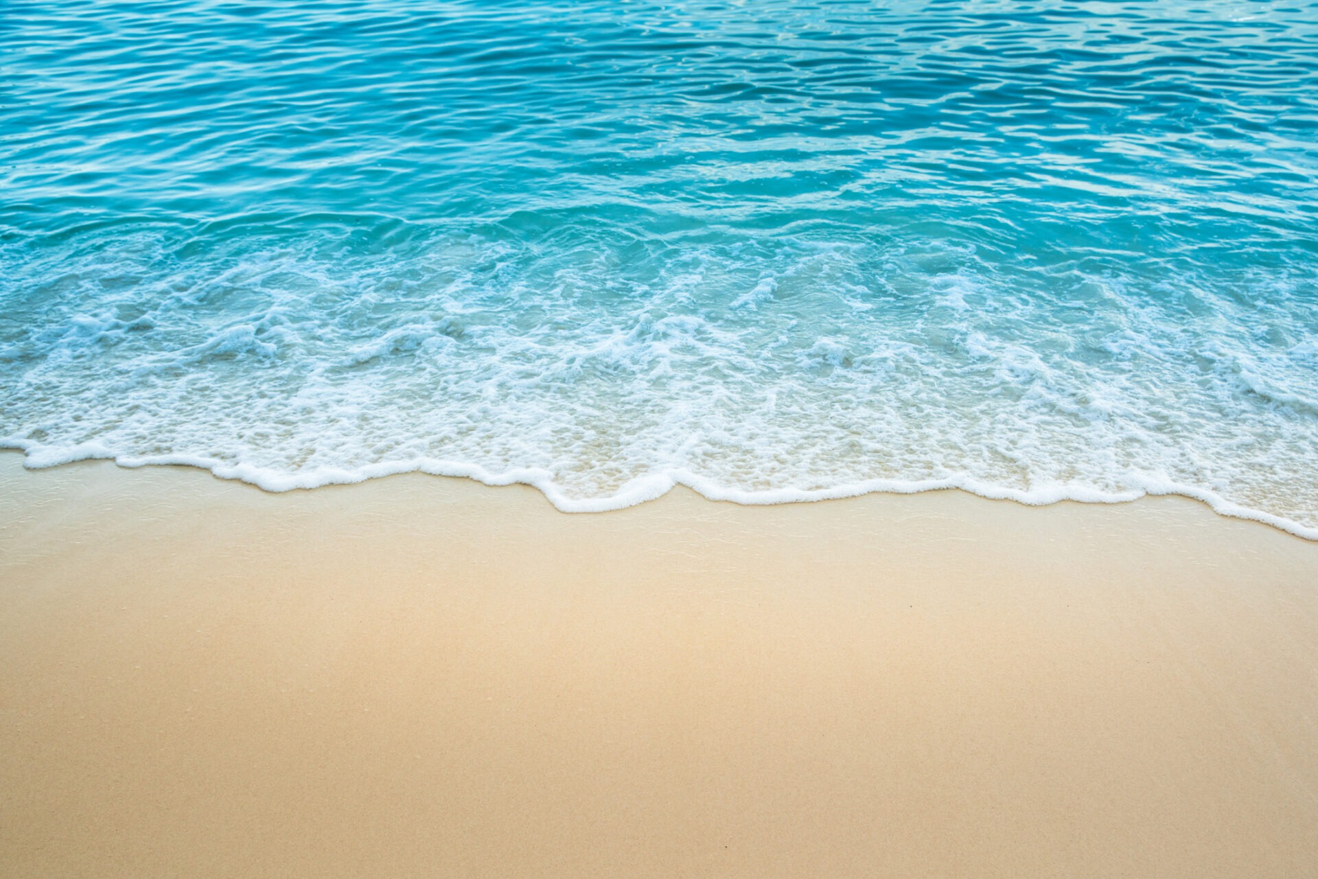 A tranquil beach scene with gentle ocean waves meeting soft sandy shore under clear blue sky, capturing a serene coastal atmosphere.