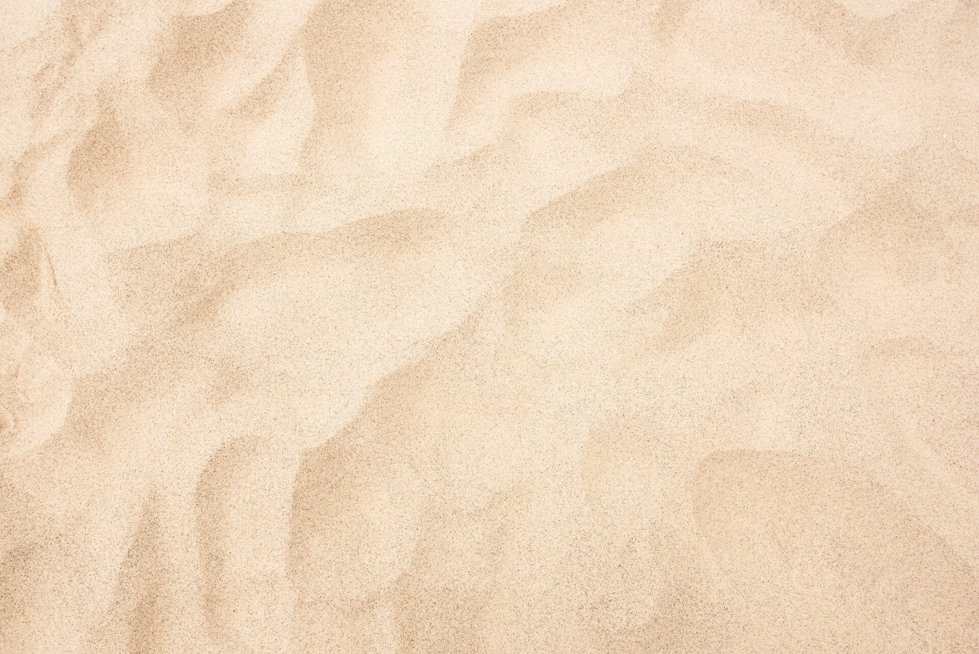 Close-up view of smooth, golden sand texture, showcasing detailed, natural wave patterns and subtle shadows. An abstract representation of a sandy surface.