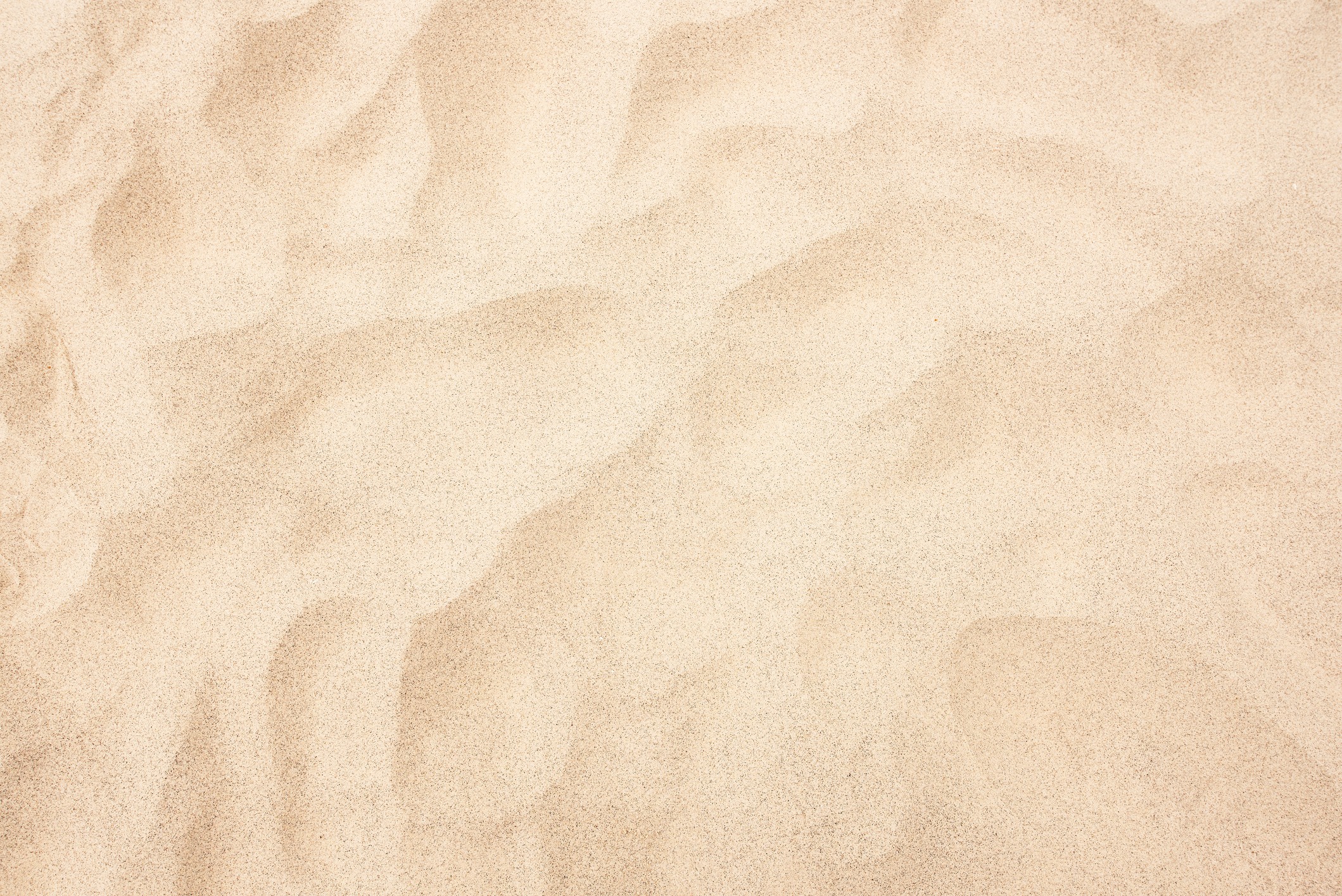 Close-up view of smooth, golden sand texture, showcasing detailed, natural wave patterns and subtle shadows. An abstract representation of a sandy surface.
