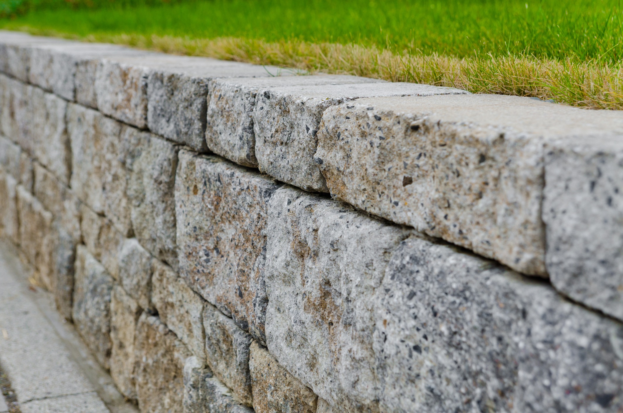 A close-up of a stone retaining wall with neatly cut stones, bordered by green grass, showcasing texture and natural tones.